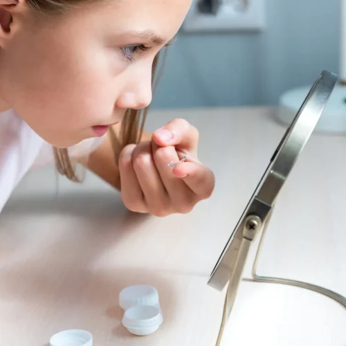 Child girl puts on contact lenses for vision at home in front of a mirror