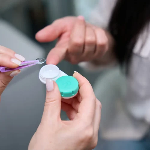 Closeup of optometrist hands removing clear contact lens out of container with tweezers in presence of patient
